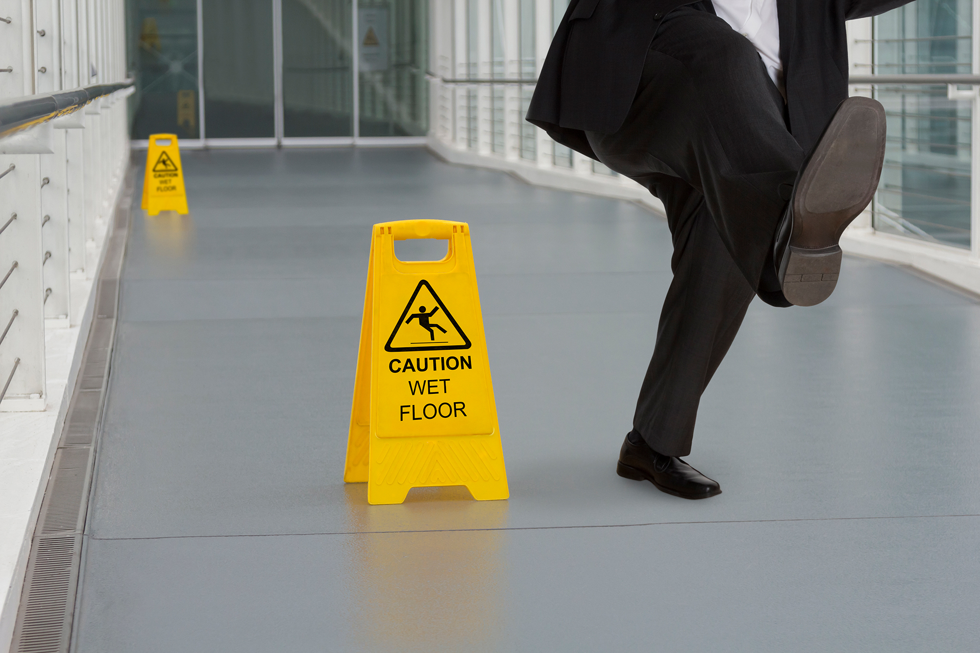 A business man slips down a corridor next to a sign indicating a slippery surface