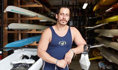 A man stands solemnly looking at the camera with canoes behind him