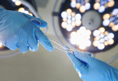 A surgeon passes another surgeon a piece of medical equipment