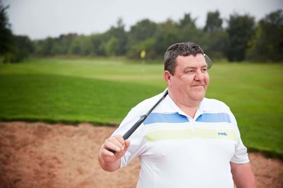 a man in a polo shirt stands on a golf course with a golf club over his shoulder