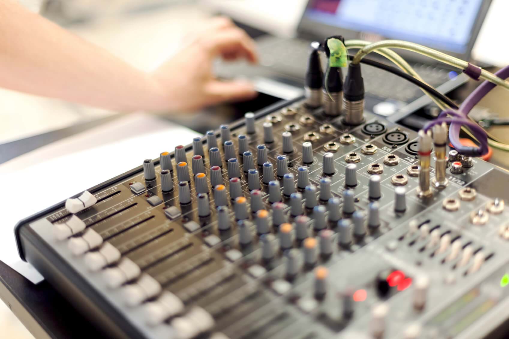 close up of sound equipment with blurred laptop and hand in background