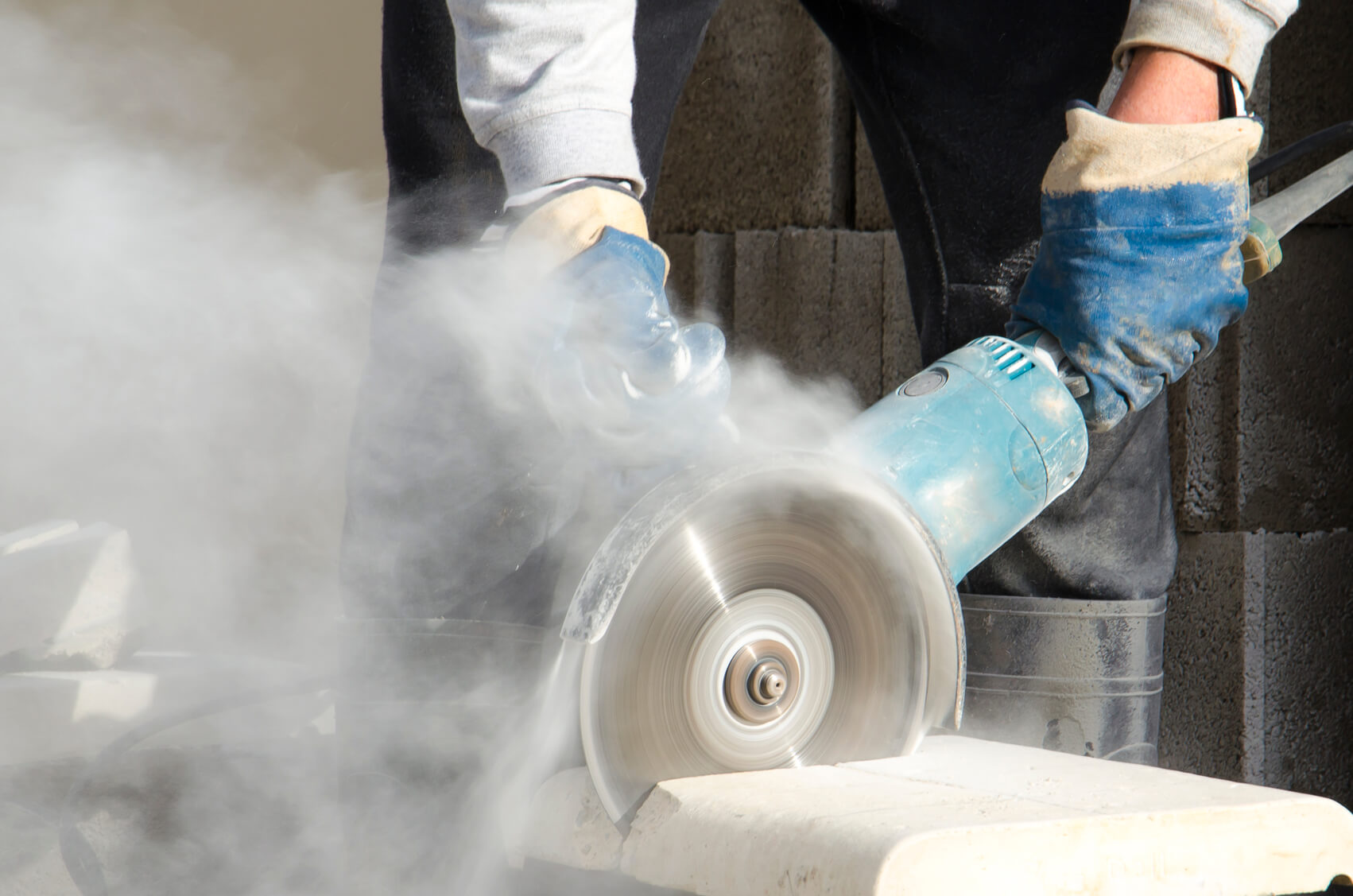 labourer using a power tool to saw through a slab causing dust debris