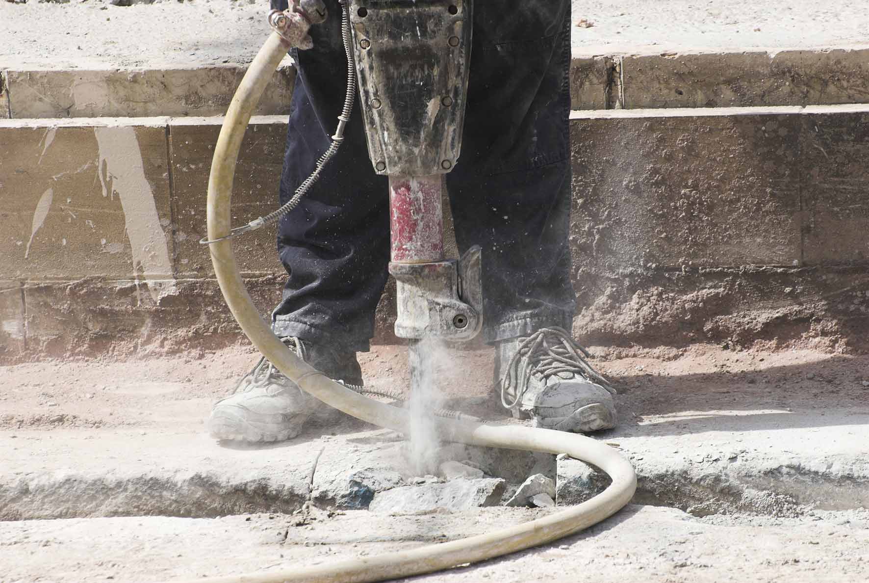 labourer using an electric drill to drill through pavement causing dust