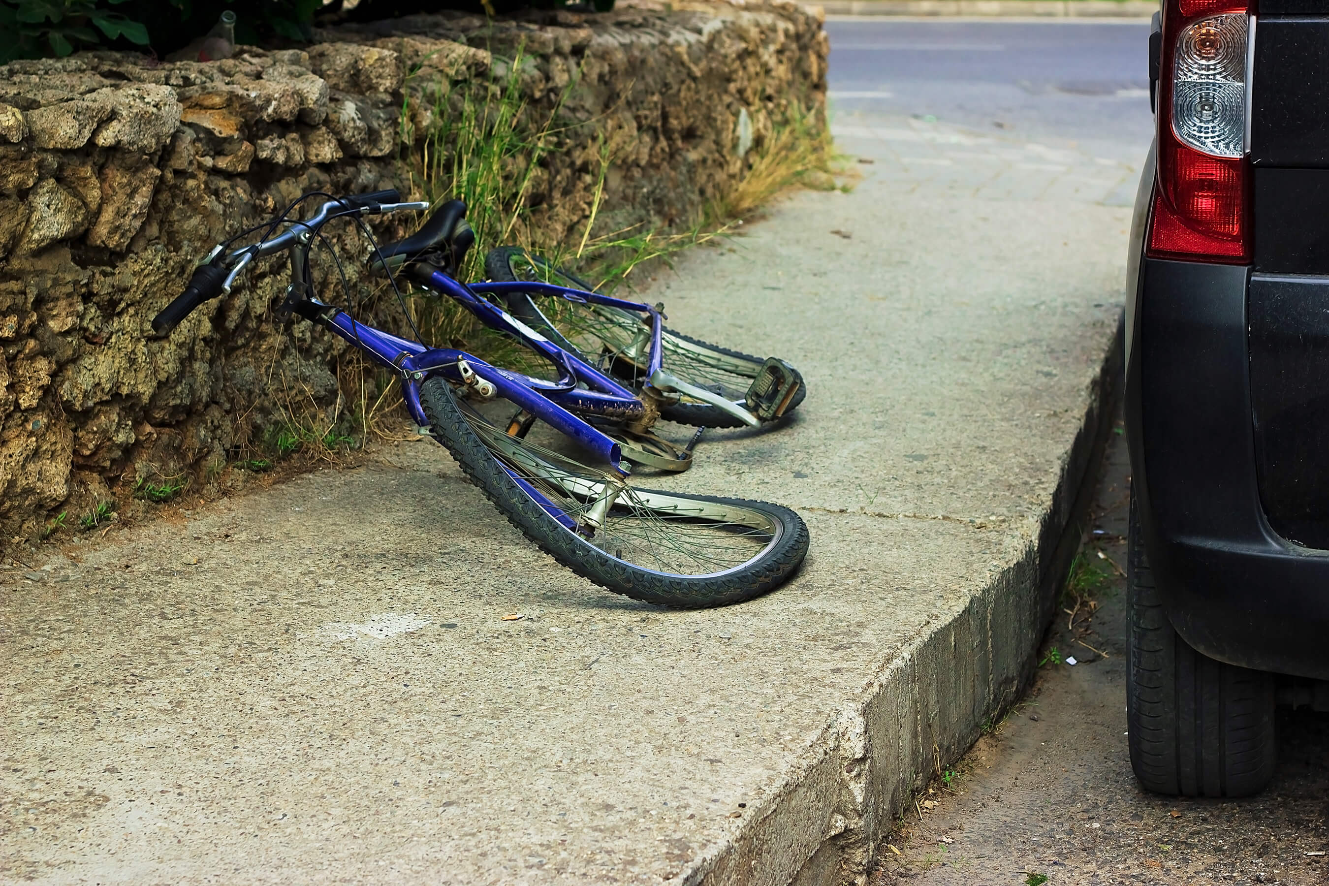 blue bicycle lying damaged on the pavement next to a black van