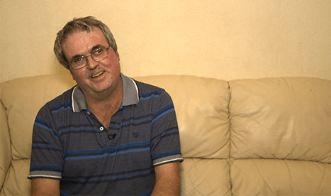 A man sits on his sofa smiling