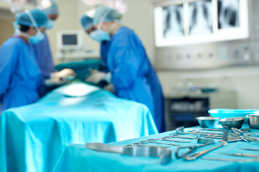 blurred image of surgery taking place with surgical equipment in focus at front of shot