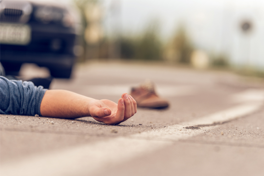 arm of a man lying face up on a road shoe and car blurred in background