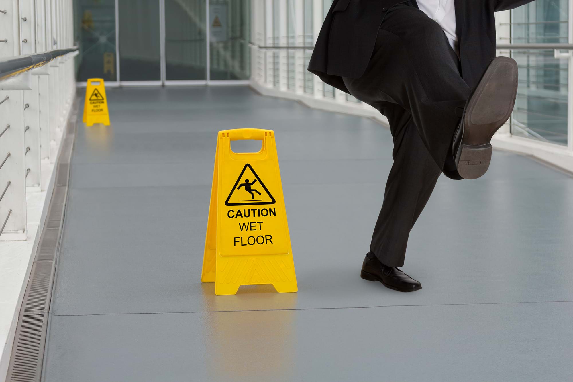 A business man slips down a corridor next to a sign indicating a slippery surface
