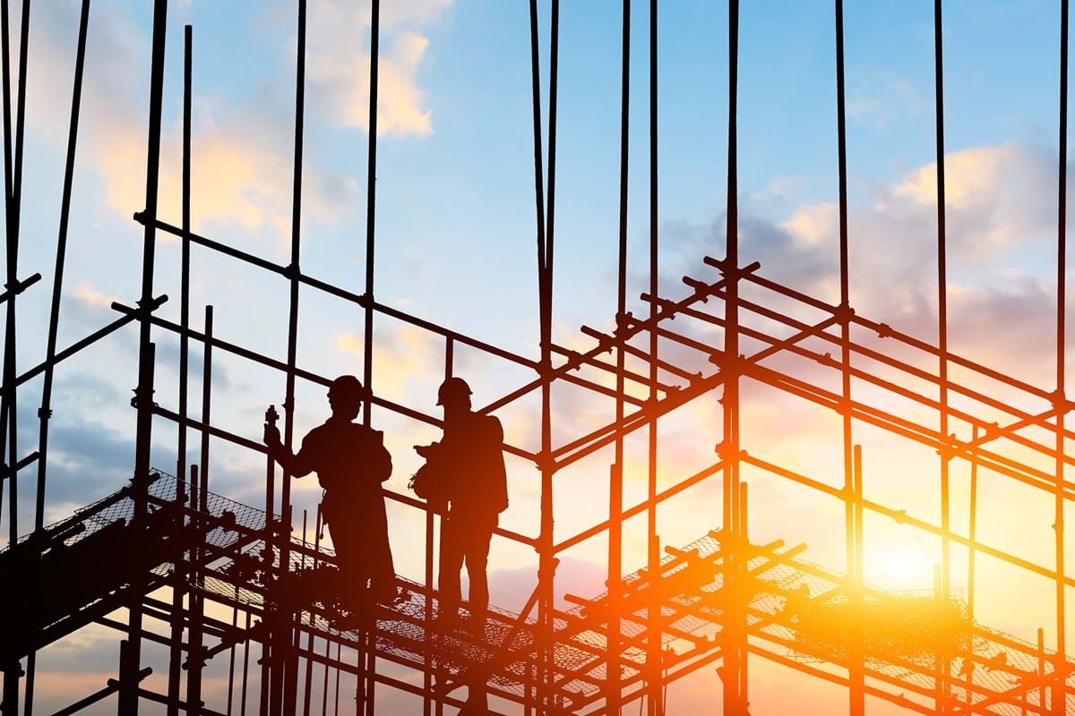 Scaffolders working at height against sunset backdrop.