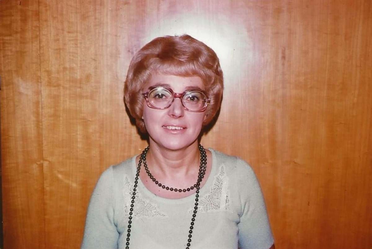 Muriel Jeffrey wearing a light blue jumper by a wooden wall
