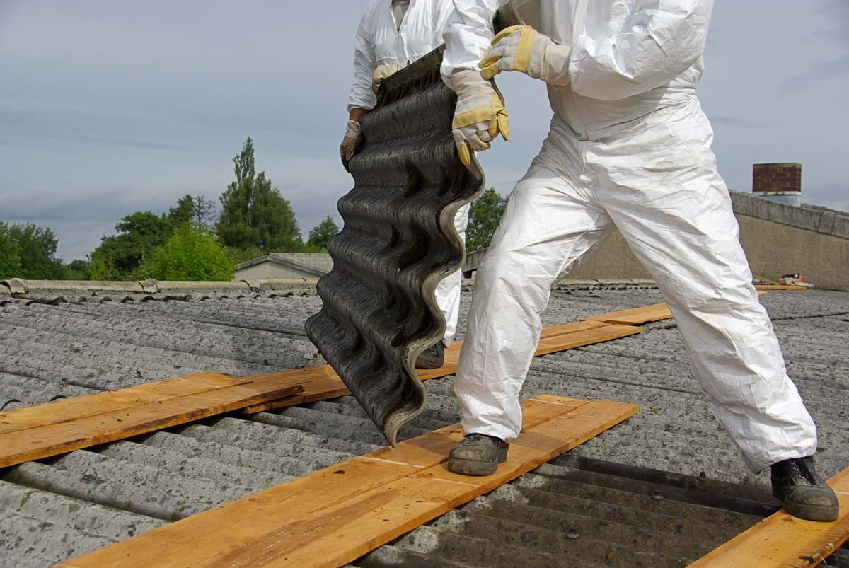 construction workers in white overalls lifting up a roof that's contaminated with asbestos.