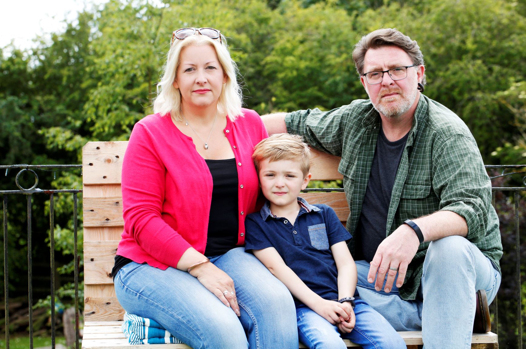 a man and woman sit on a bench with their son in the middle of them