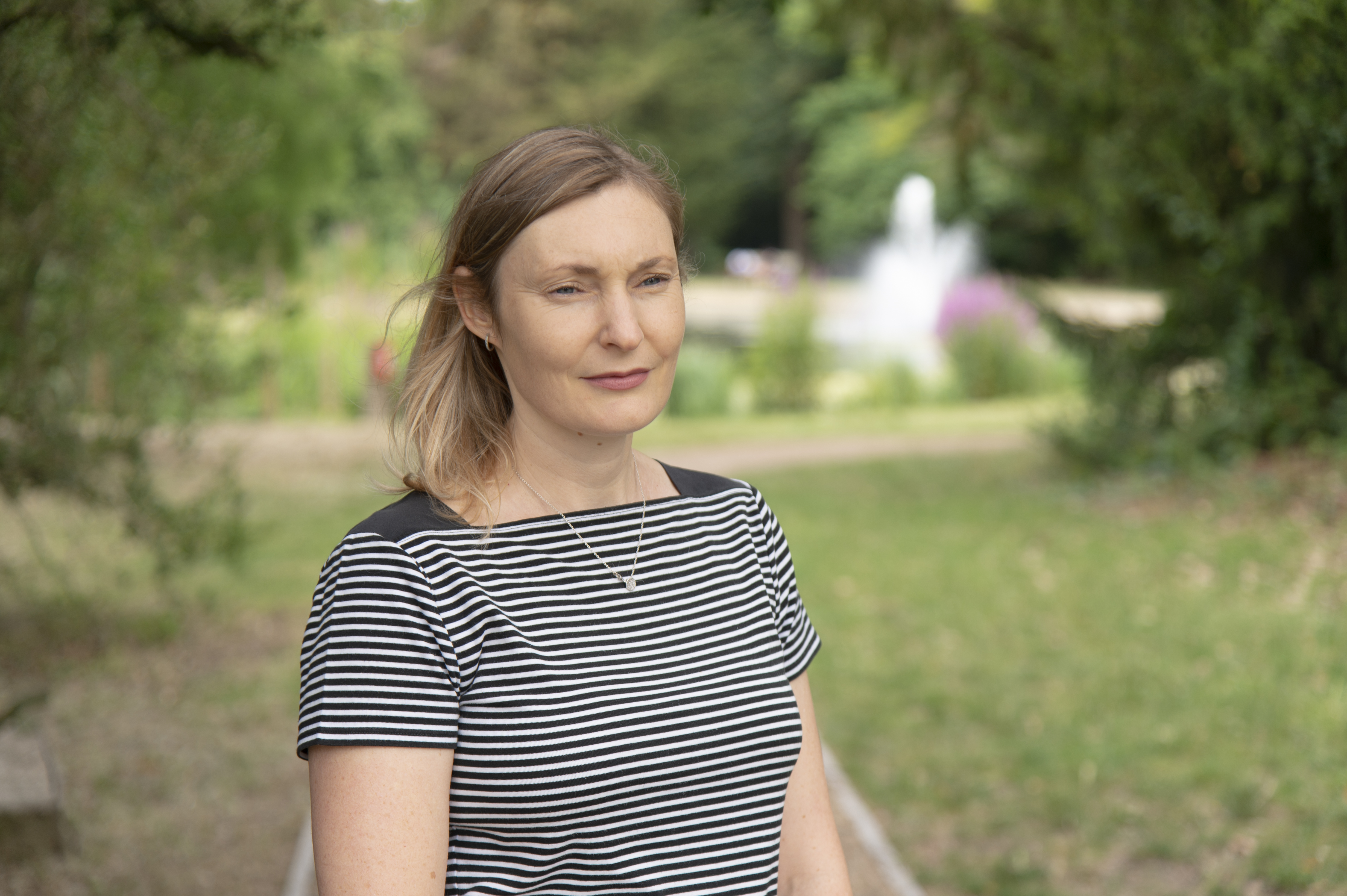 A lady in a striped top stands outside looking into the distance