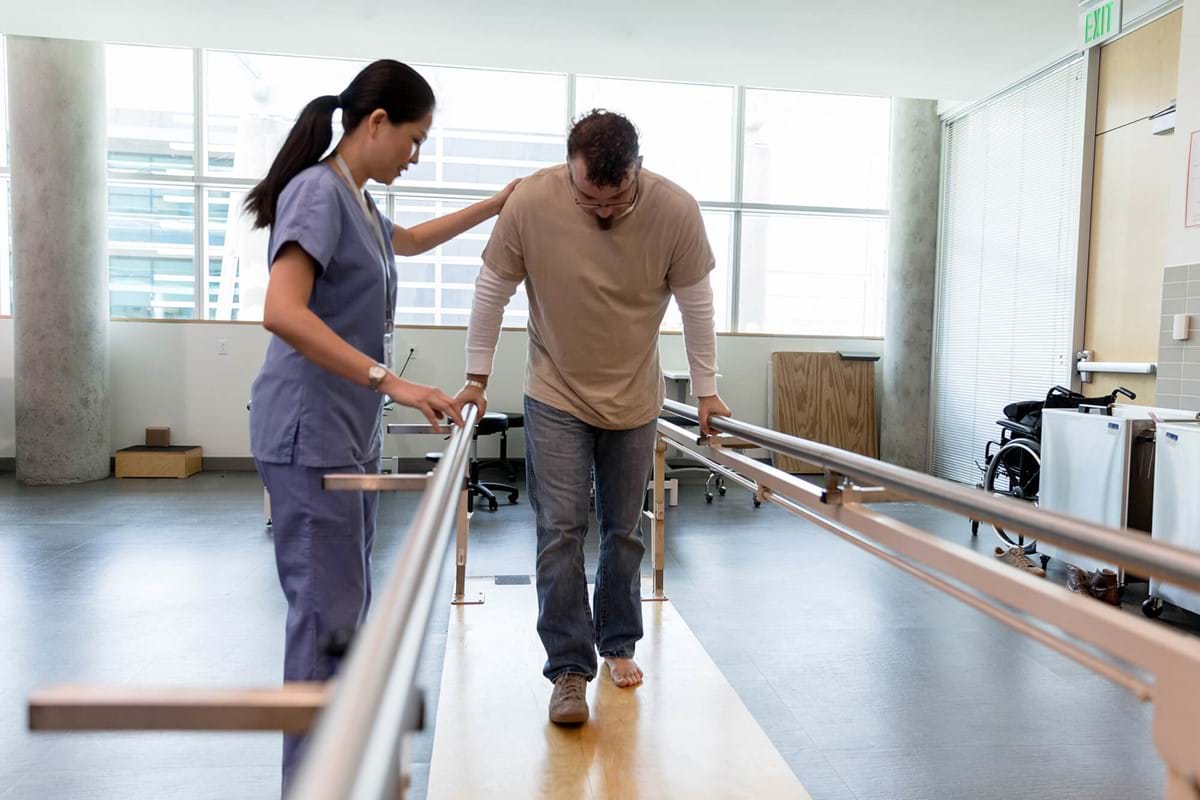 A man using paralell bars to help teach him how to walk