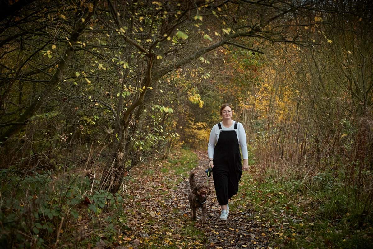A woman walking a dog in the woods